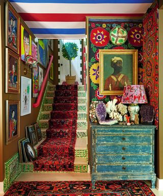 a hallway with a staircase with a patterned carpet and a runner and lots of art on the wall